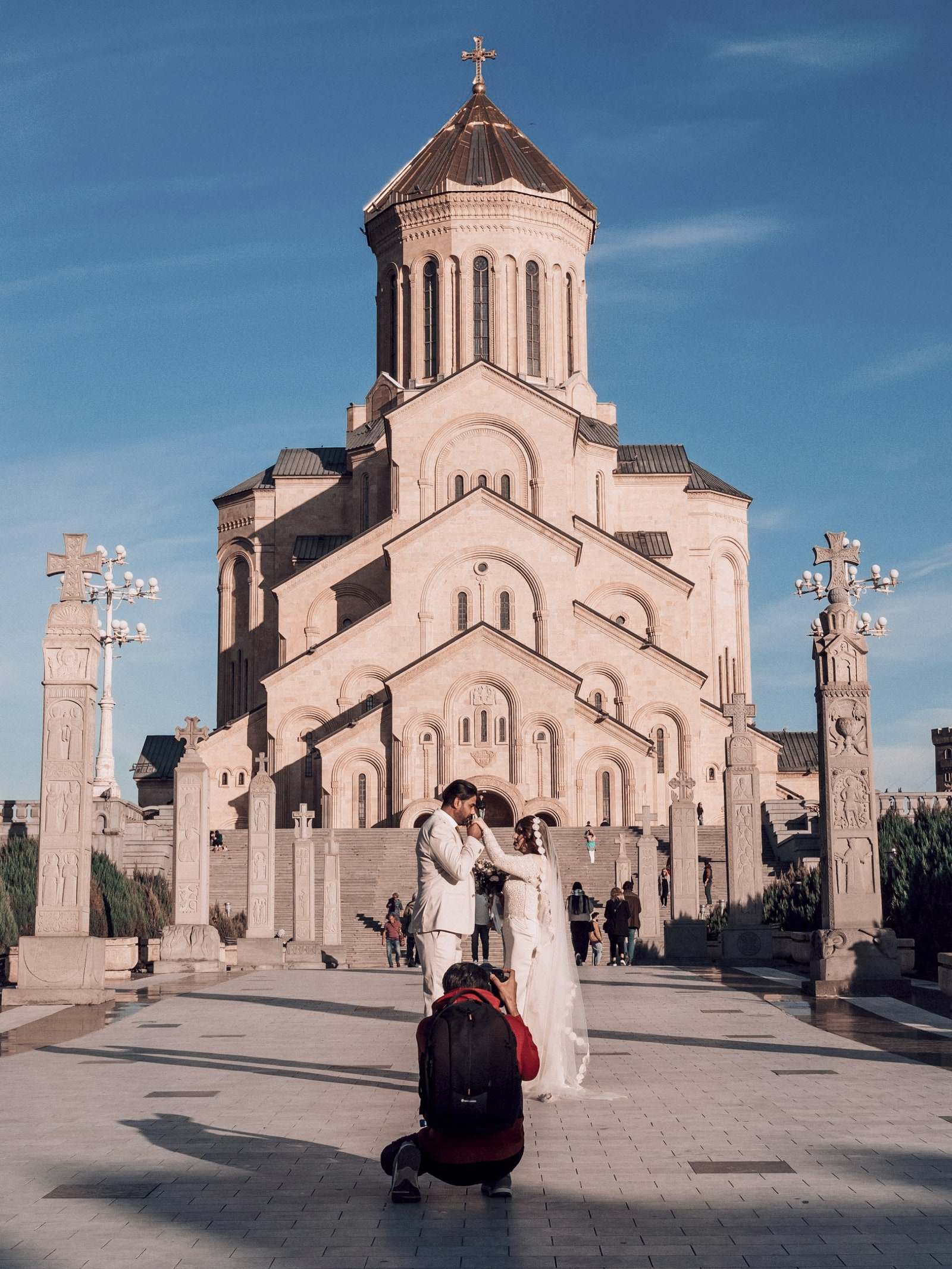 A bride and groom on the steps of the Holy Trinity Cathedral in Tbilisi, the cathedral rising behind them